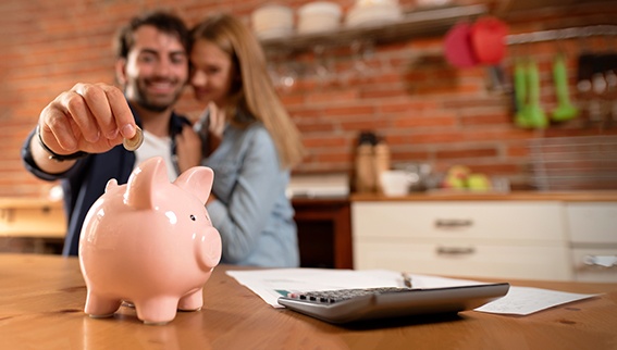 Paar in der Küche ist glücklich, weil es Geld sparen kann. Er wirft Geld in das im Vordergrund stehende Sparschwein